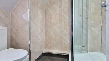 A modern bathroom with a toilet, a shower with glass doors, and marble walls.