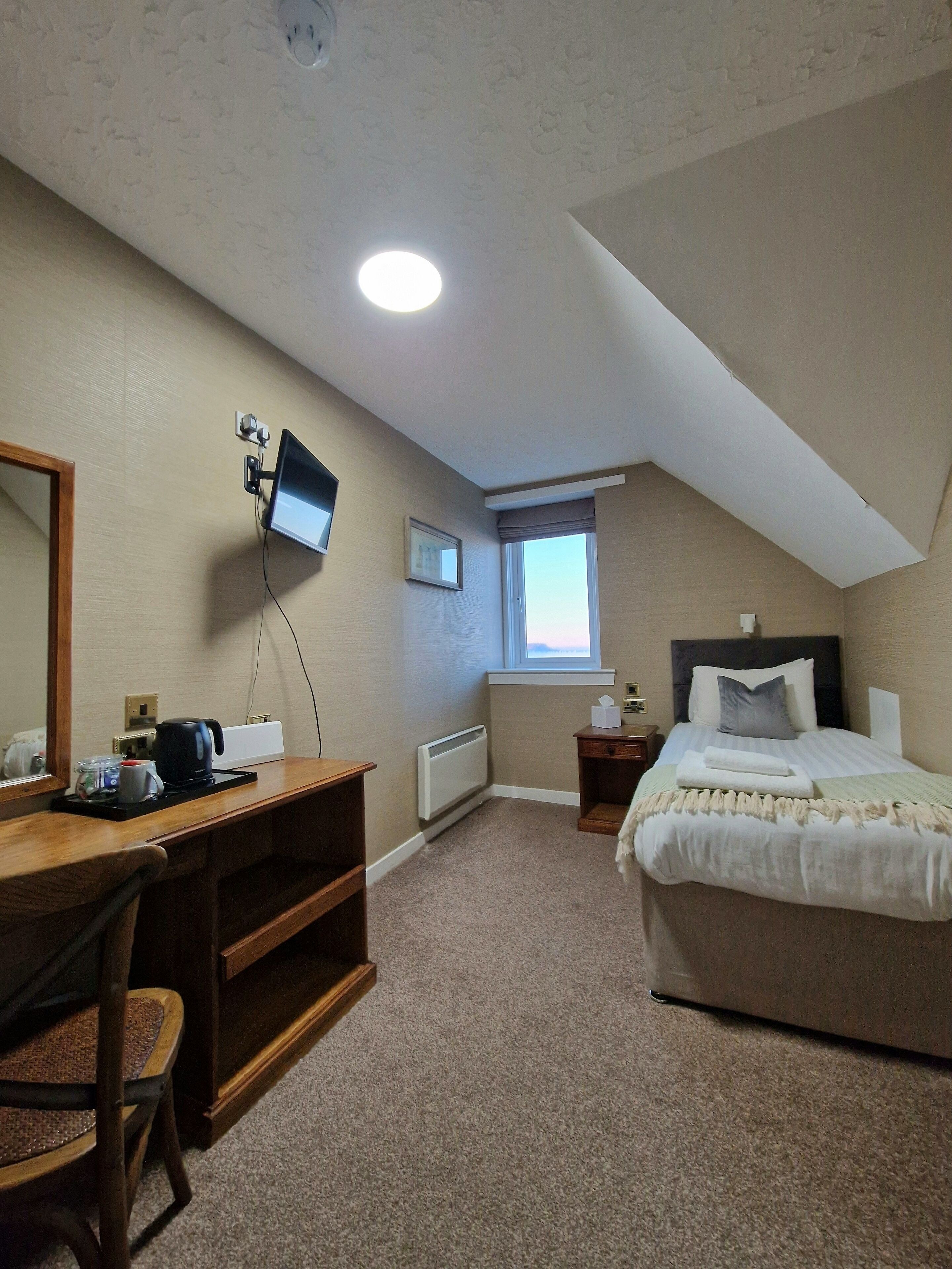 A bedroom with a bed, a desk with a computer, a chair, a window, and a radiator.