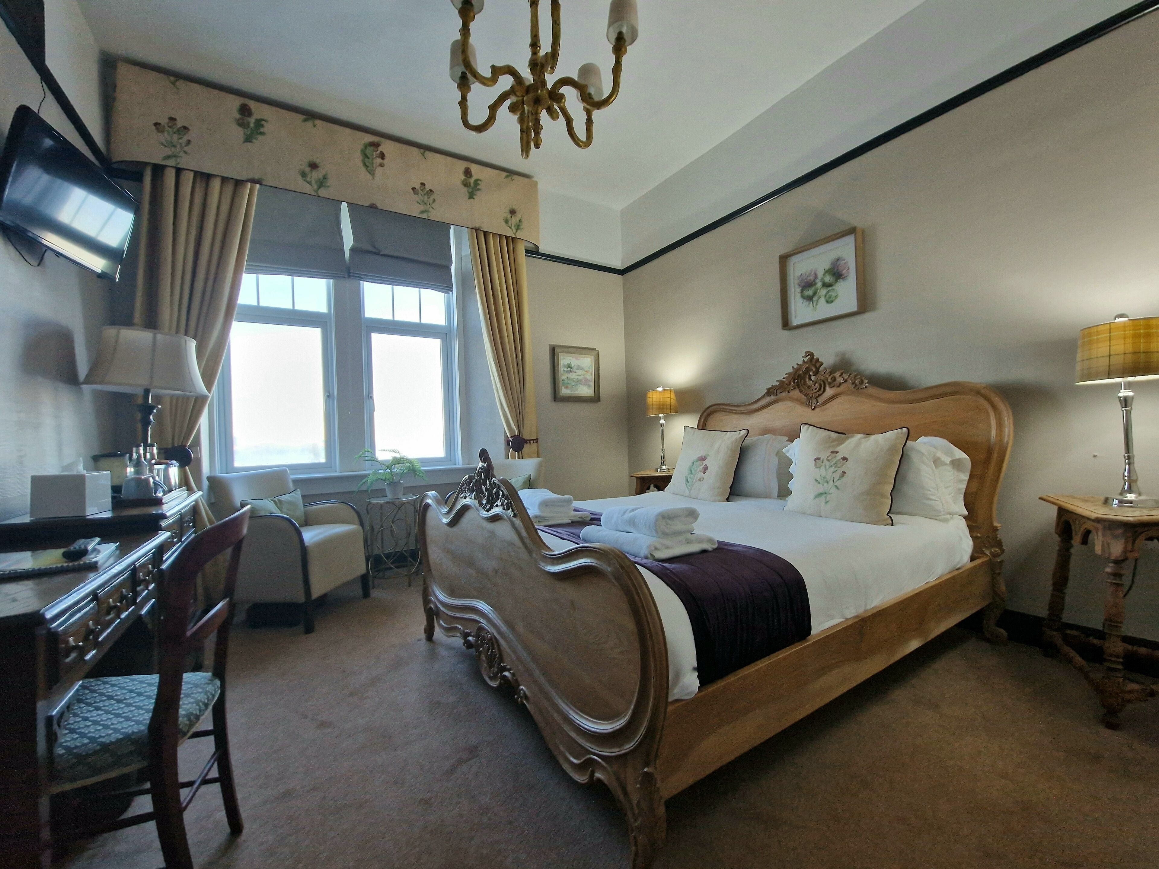 A hotel room with a large bed, a desk, a chair, a television, and a chandelier.