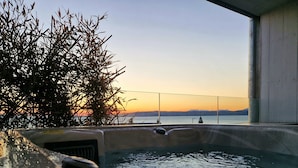 A hot tub with a view of a sunset over water, surrounded by foliage. - West Highland Hotel (Mallaig)