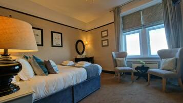 Una habitación de hotel con cama, dos sillas, escritorio, lámpara y ventana con cortinas.