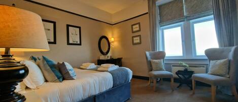 A hotel room with a bed, two chairs, a desk, a lamp, and a window with curtains.