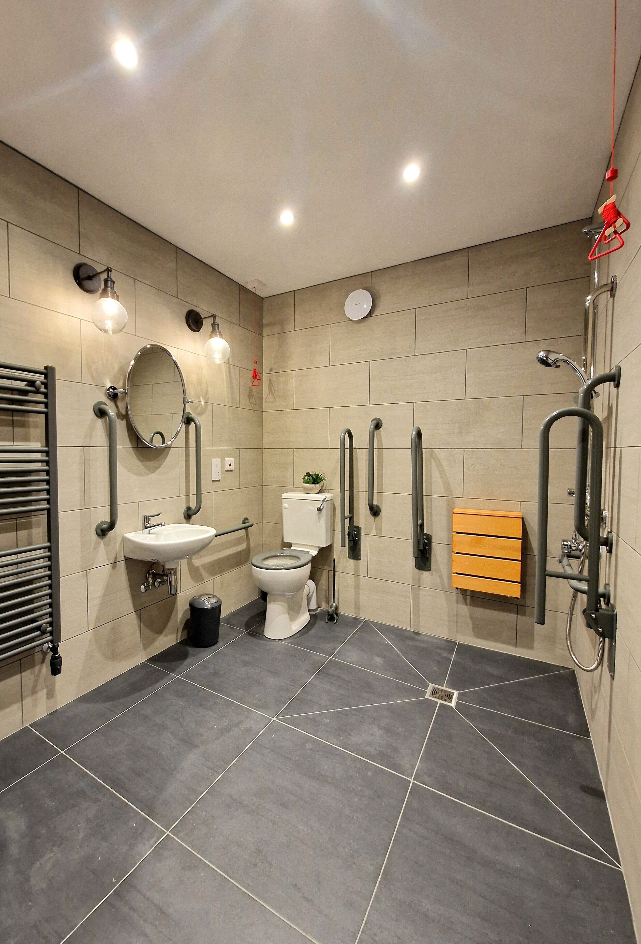 A modern bathroom with a toilet, sink, and shower area, equipped with grab bars and a mirror.