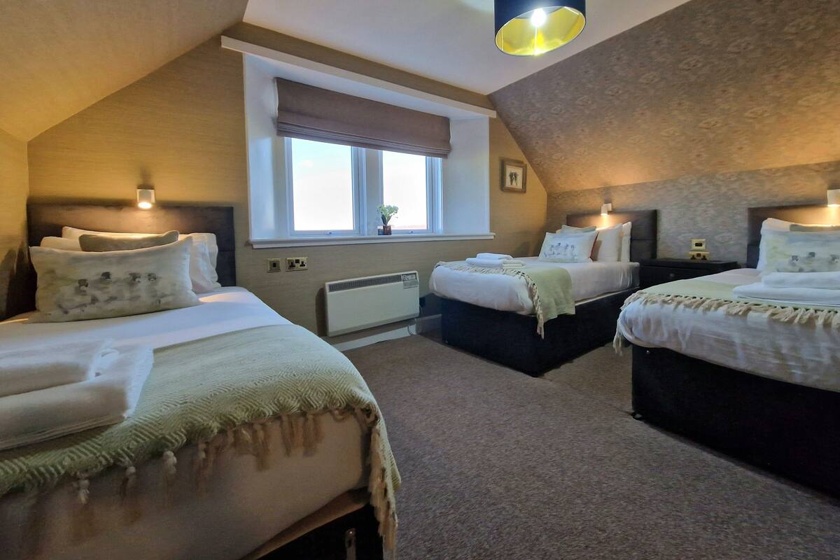 A bedroom with two beds, a window with blinds, a radiator, and a ceiling light fixture.