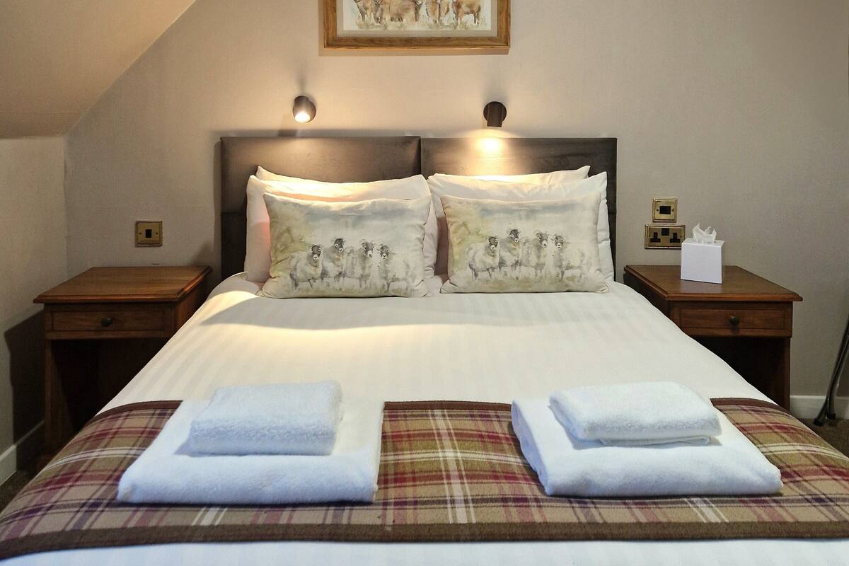 A neatly made bed with two pillows, a bedside table with a lamp, and a framed picture on the wall.
