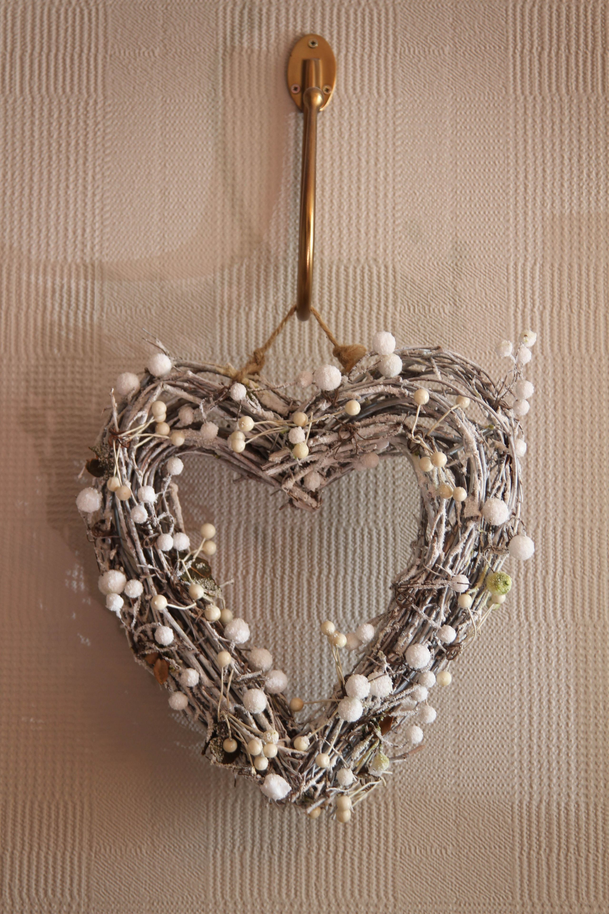 A heart-shaped wreath with white and green berries hanging on a textured wall.