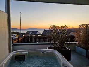Un jacuzzi en una azotea con vistas a una puesta de sol y montañas lejanas.