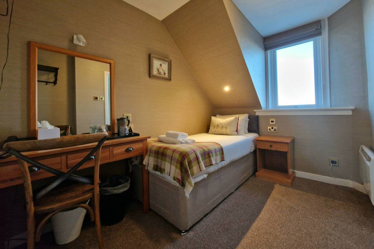 A bedroom with a bed, a desk, a chair, a mirror, a window, and a picture on the wall.