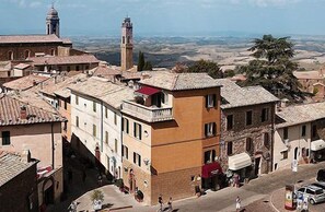 A historic town with traditional architecture, including a prominent tower and a street with pedestrians. - Il Barlanzone (Montalcino)