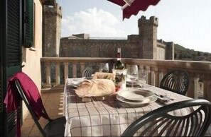 A table set for two with a checkered tablecloth, plates, glasses, and a bottle of wine, overlooking a historic stone wall and a clear sky. - Il Barlanzone (Montalcino)