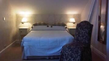 Una habitación de hotel pequeña y tenuemente iluminada, con una cama individual, dos lámparas de noche, una silla y un espejo en la pared.