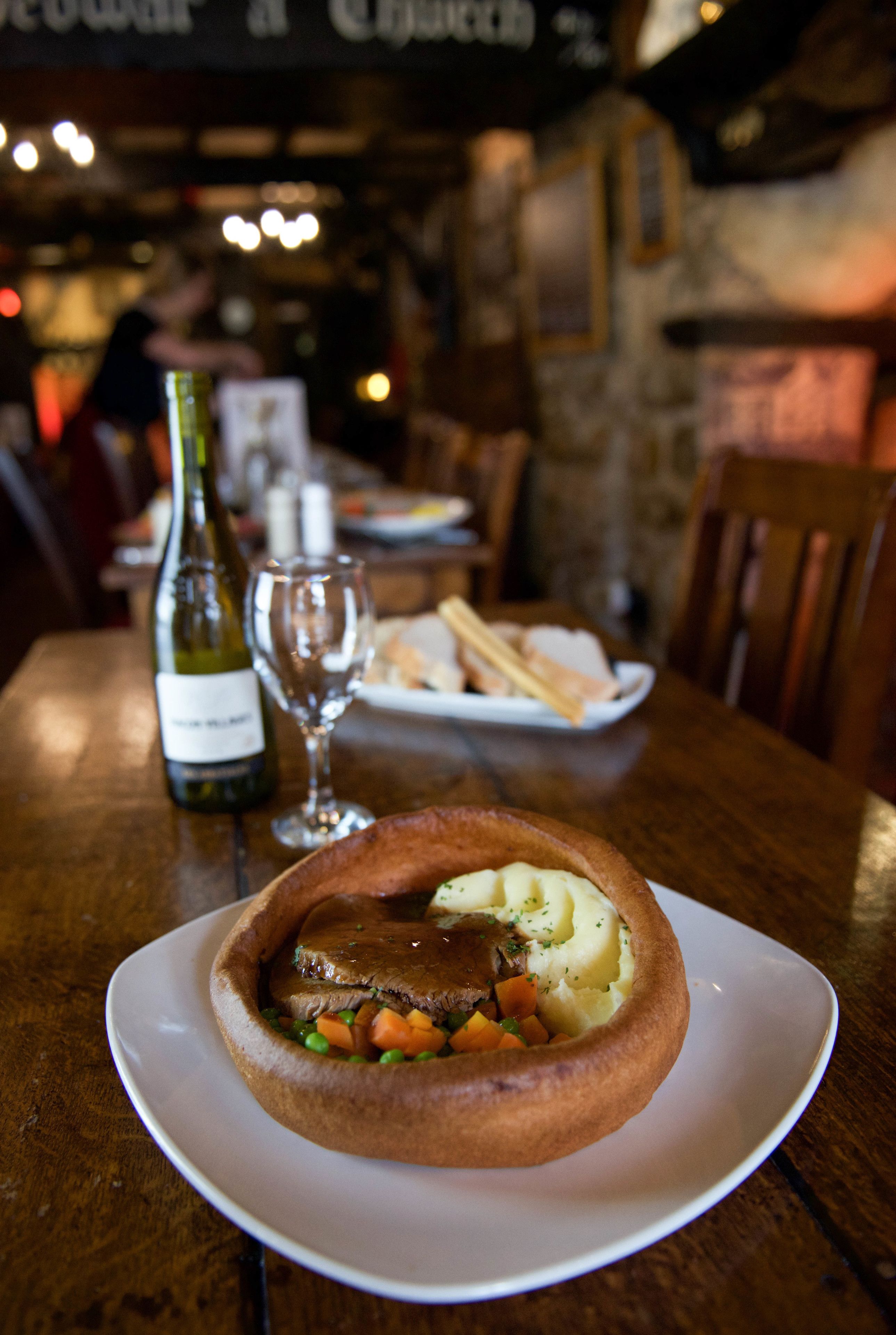 A traditional pub setting with a focus on a meal consisting of a meat pie and mashed potatoes, accompanied by a bottle of wine and a glass.