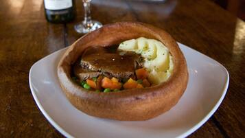 A traditional pub setting with a focus on a meal consisting of a meat pie and mashed potatoes, accompanied by a bottle of wine and a glass.