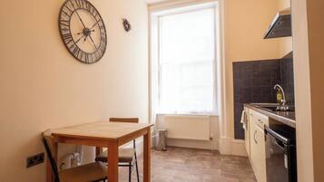 A small kitchen with a wooden table, a clock, a window, and a sink.