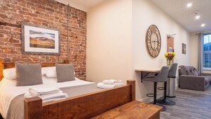 A modern bedroom with a wooden bed, a brick wall, a desk, and a sofa. - Black Boy Inn (Caernarfon)
