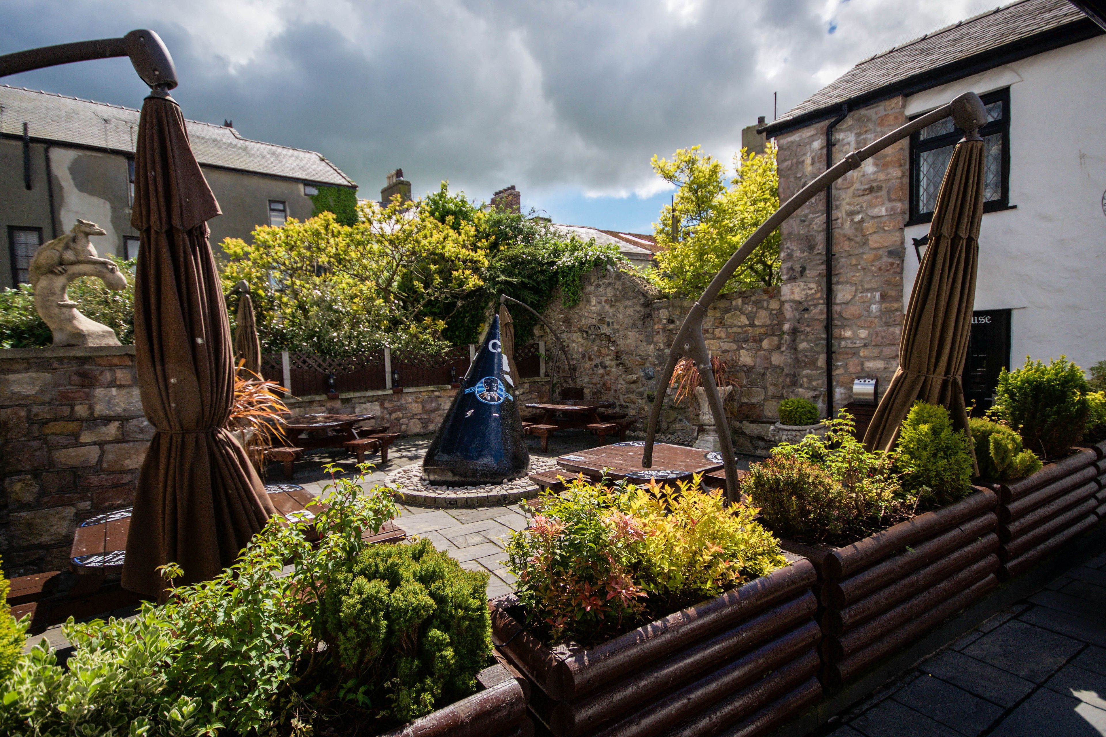 A courtyard with stone walls, a central blue sculpture, and surrounding greenery.