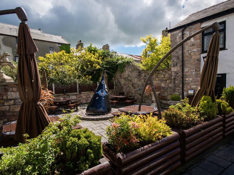 A courtyard with stone walls, a central blue sculpture, and surrounding greenery.