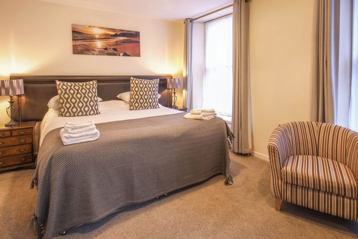 Ein Hotelzimmer mit einem großen Bett, einem Sessel, einem Nachttisch und einem Bild an der Wand.