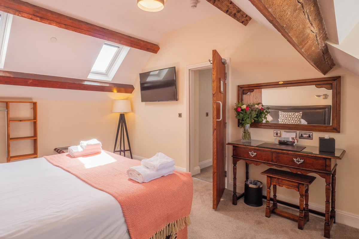 Ein Hotelzimmer mit einem Bett, einem Schreibtisch mit Spiegel, einer Lampe und einem kleinen Mülleimer.