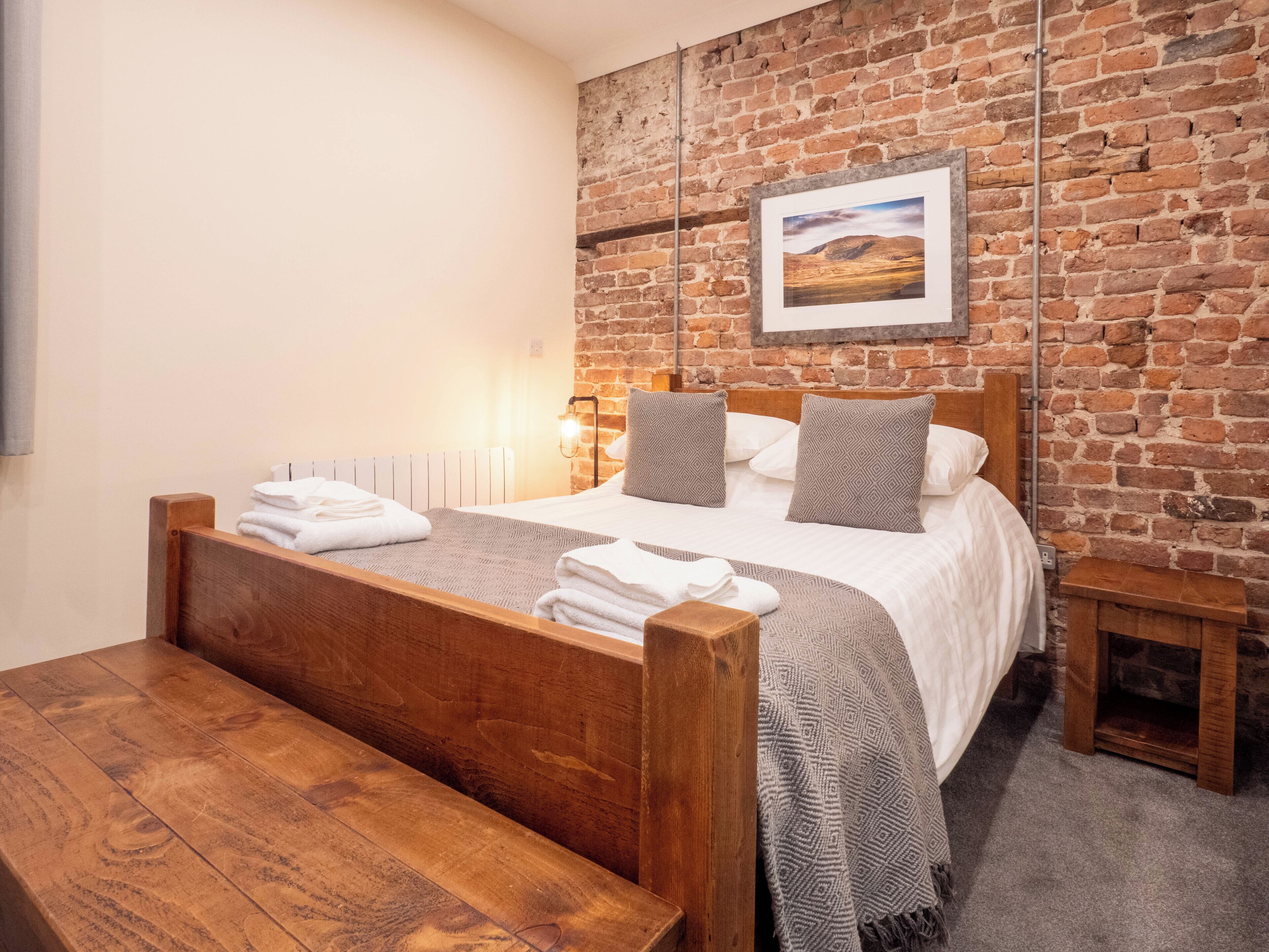 A bedroom with a wooden bed, a brick wall, and a framed picture.