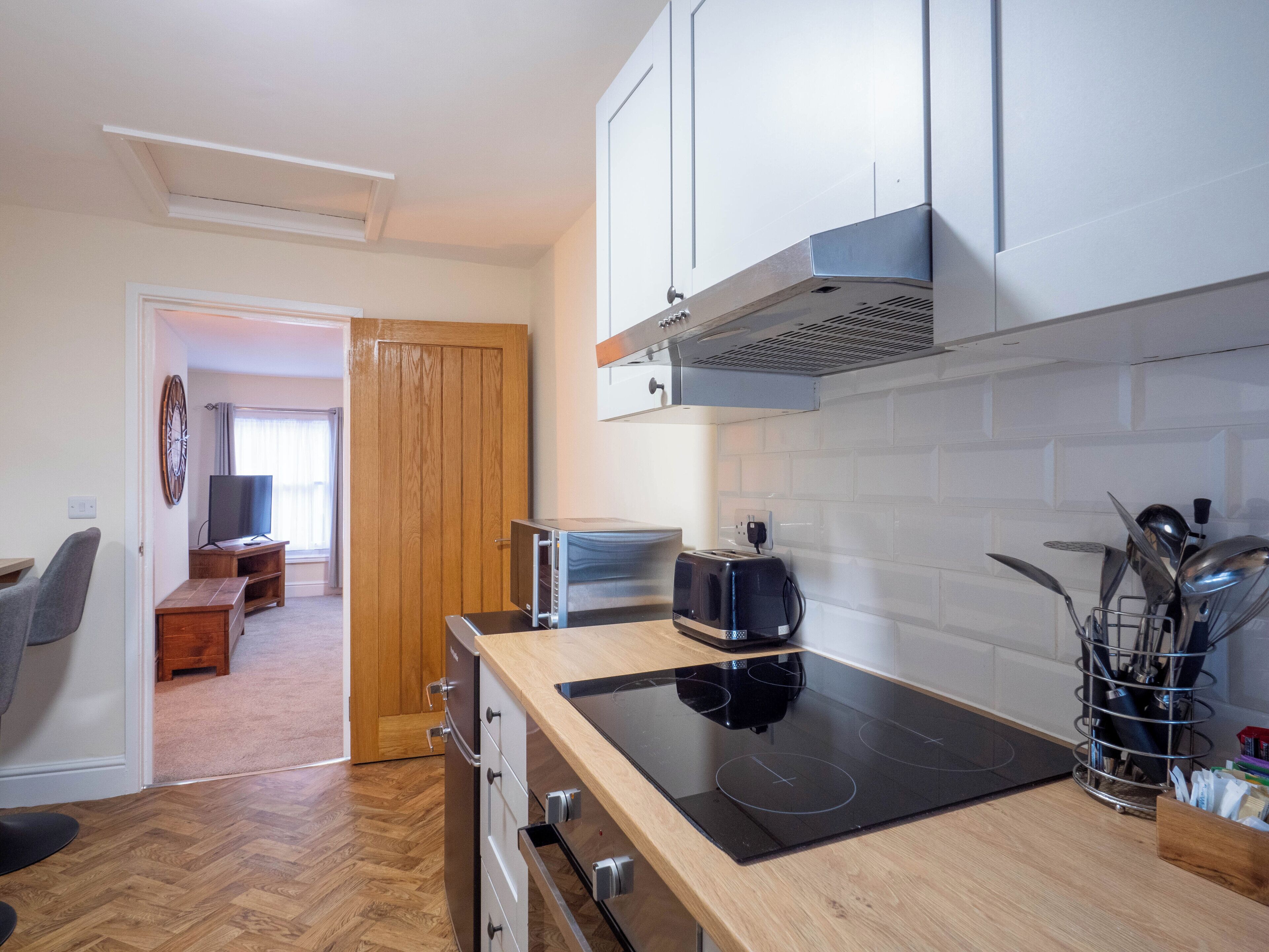Een moderne keuken met een ingebouwde kookplaat, houten keukenkastjes en een eethoek met een tafel en stoelen.