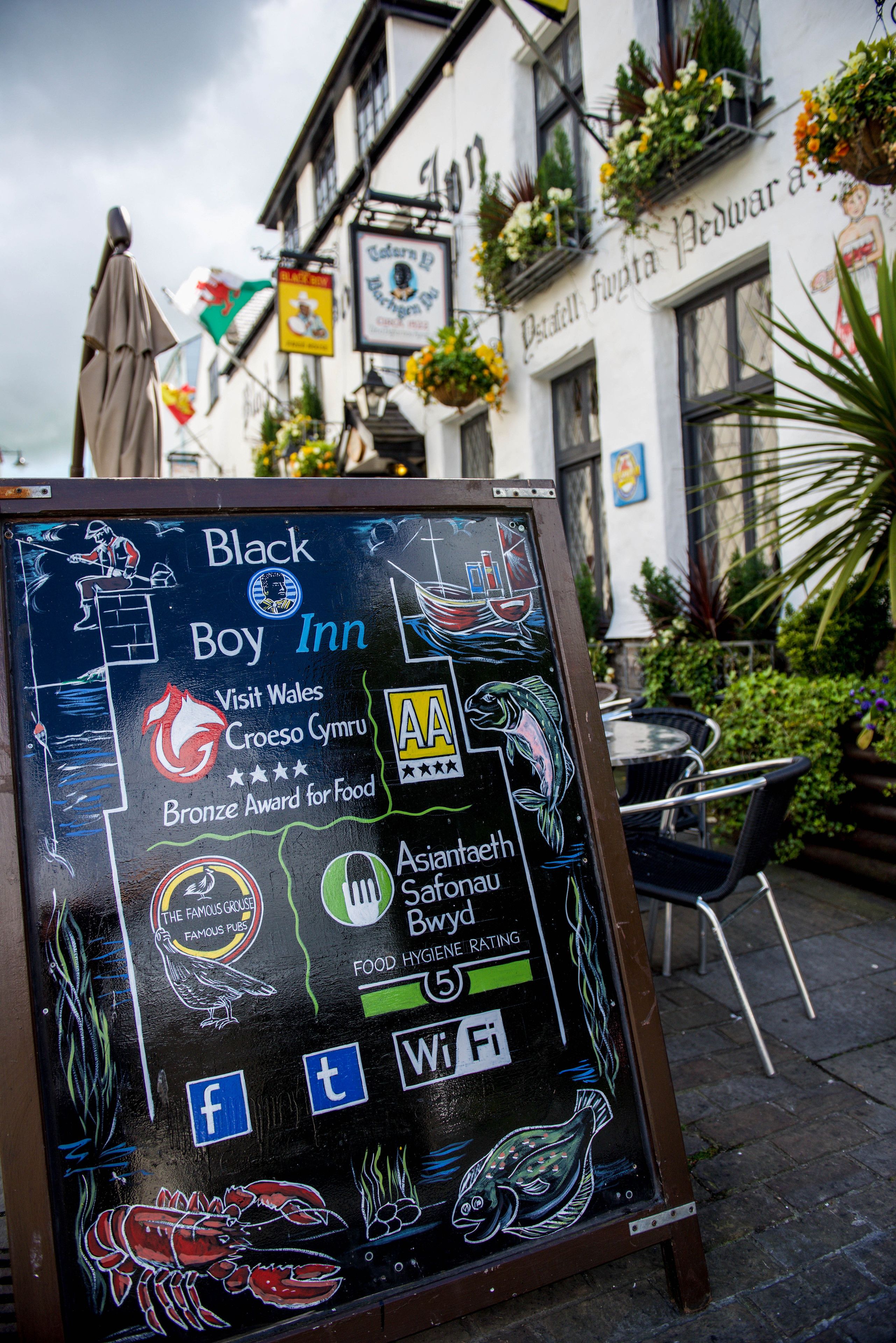 A chalkboard sign for Black Boy Inn with various awards and social media icons.