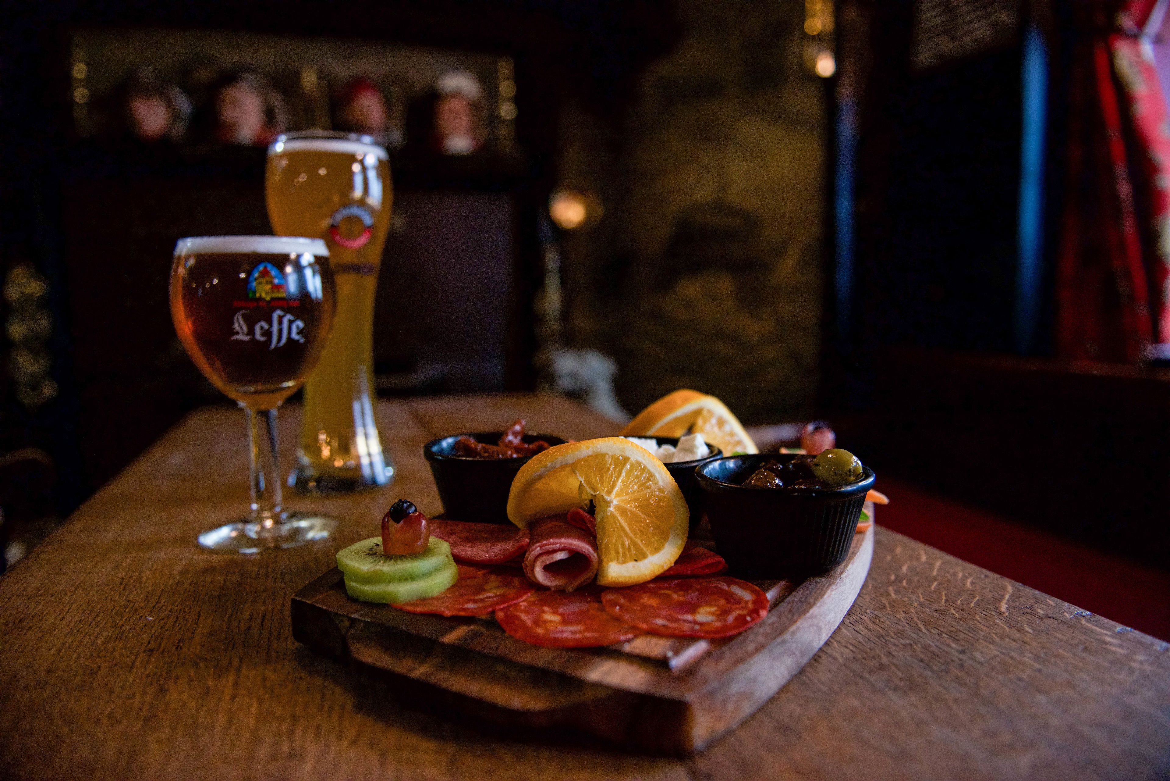 A wooden table with a variety of food items and drinks, including sliced meats, fruits, and a glass of beer.