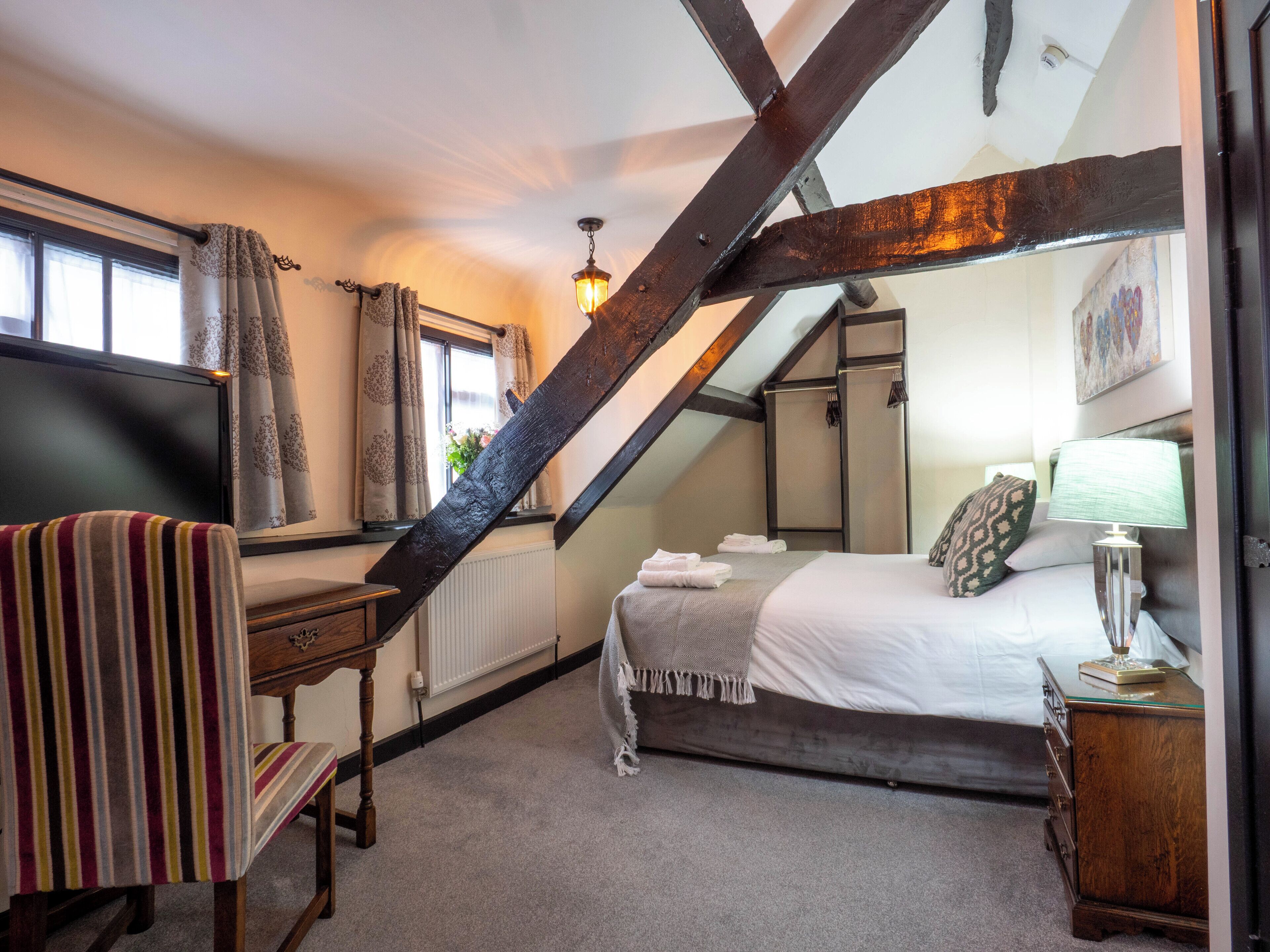 A bedroom with a bed, a desk, a chair, a lamp, and a window with curtains.