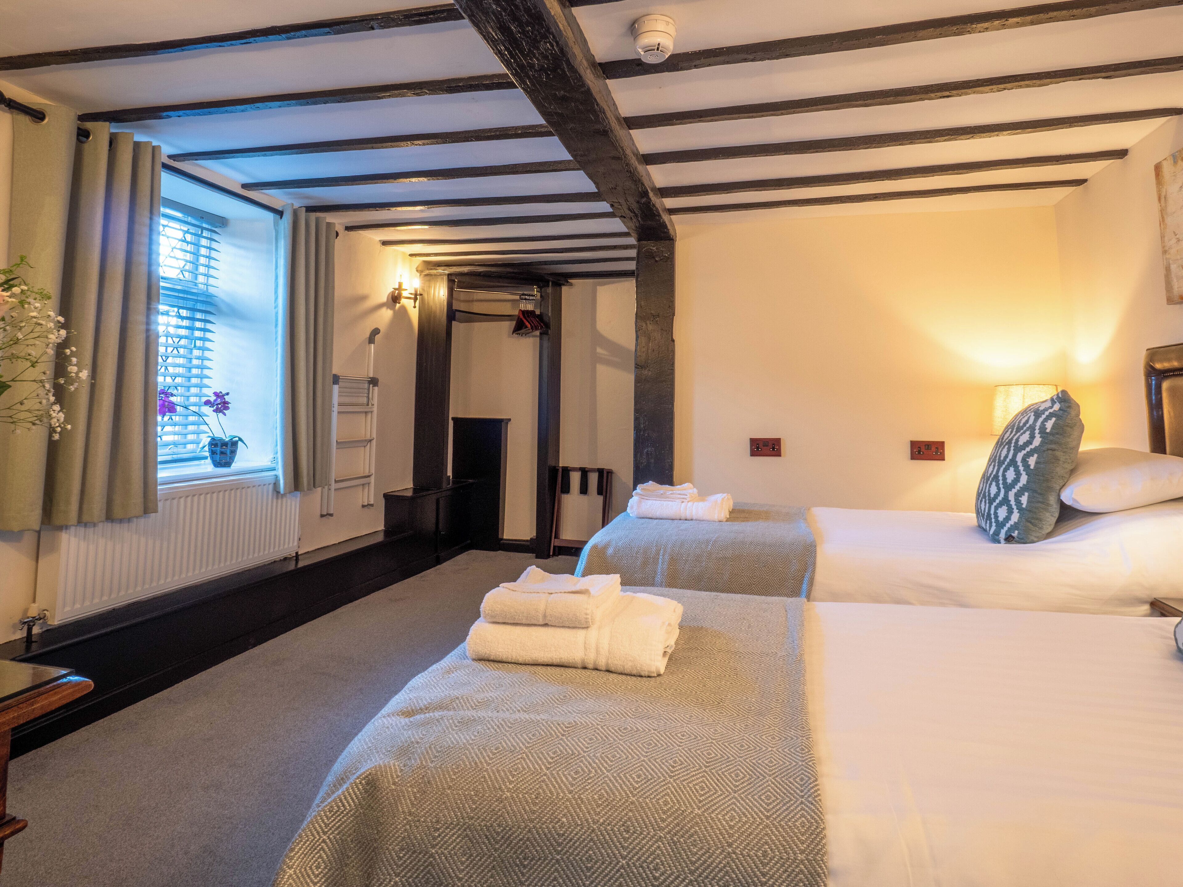 A hotel room with two beds, a window with curtains, a radiator, and a lamp.