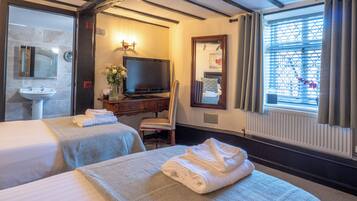 Habitación de hotel con dos camas, un televisor, un escritorio con un florero y un espejo, además de una ventana con cortinas.