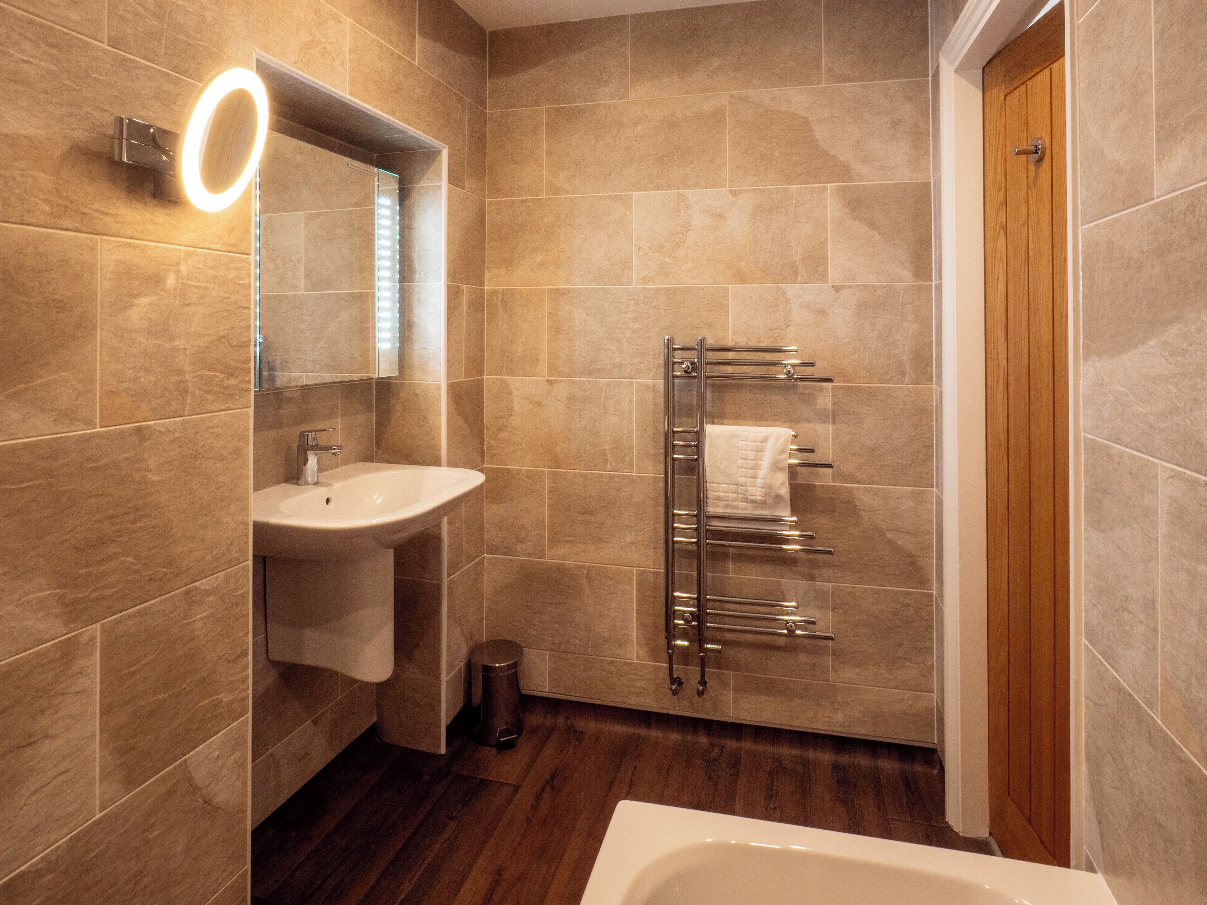Un baño moderno con lavamanos, espejo, toallero y puerta de madera.