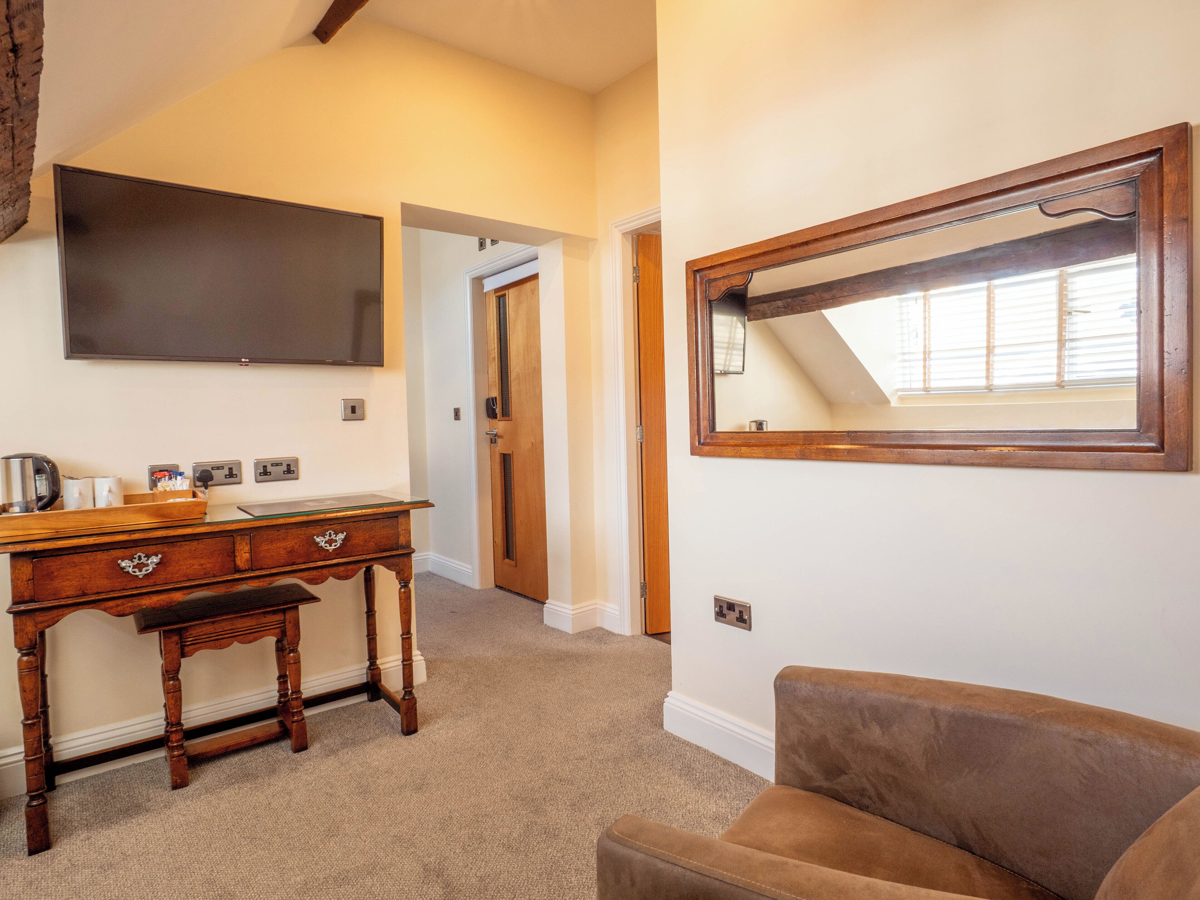 A hotel room with a wooden desk, a brown sofa, a large mirror, and a flat-screen TV.