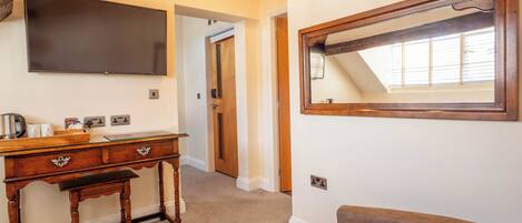 A hotel room with a wooden desk, a brown sofa, a large mirror, and a flat-screen TV.