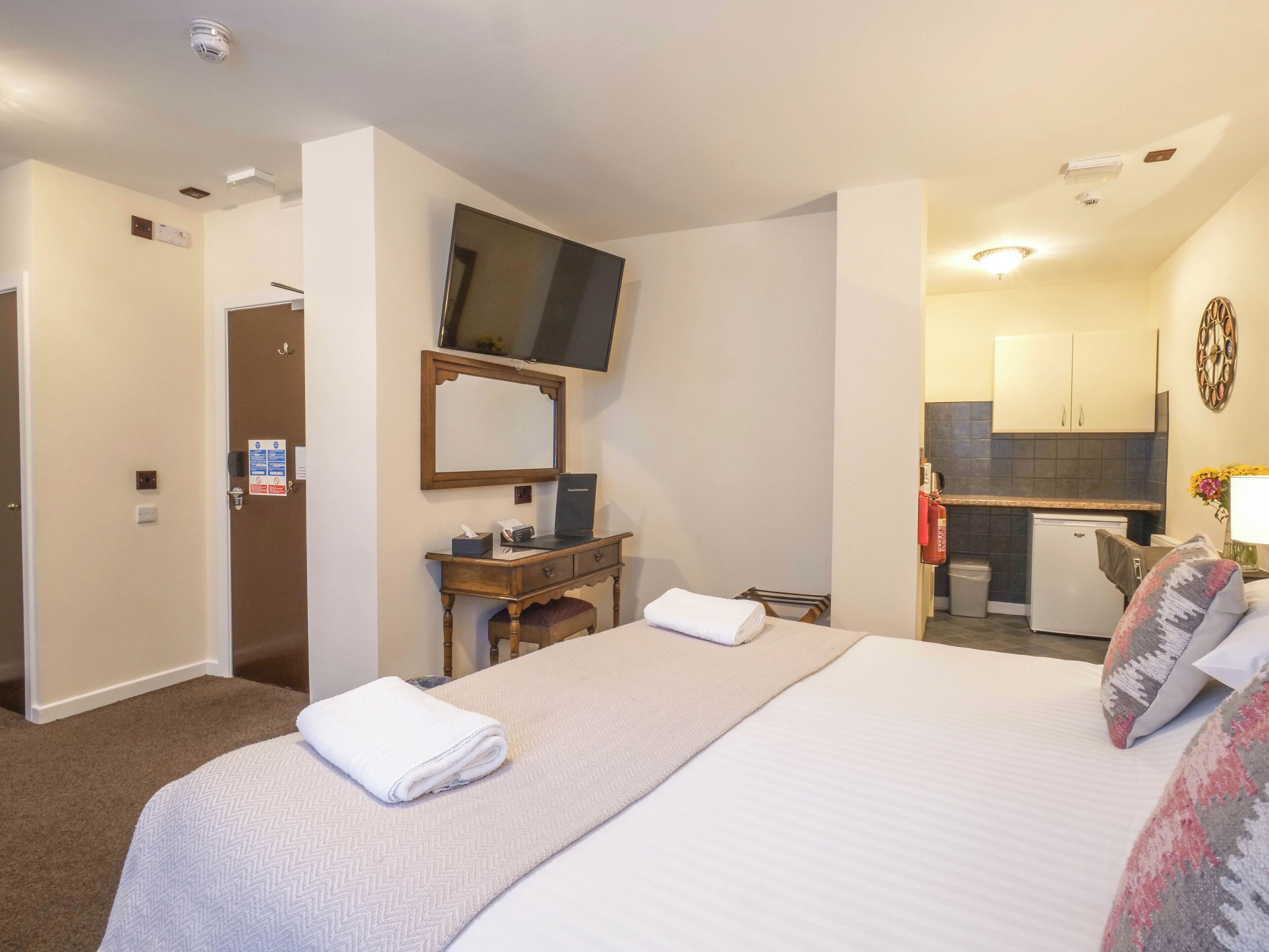 A hotel room with a bed, a desk with a computer, a television, a small kitchenette, and a bathroom.