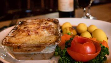 A plate with a baked dish, a bottle of wine, and a glass on a table.