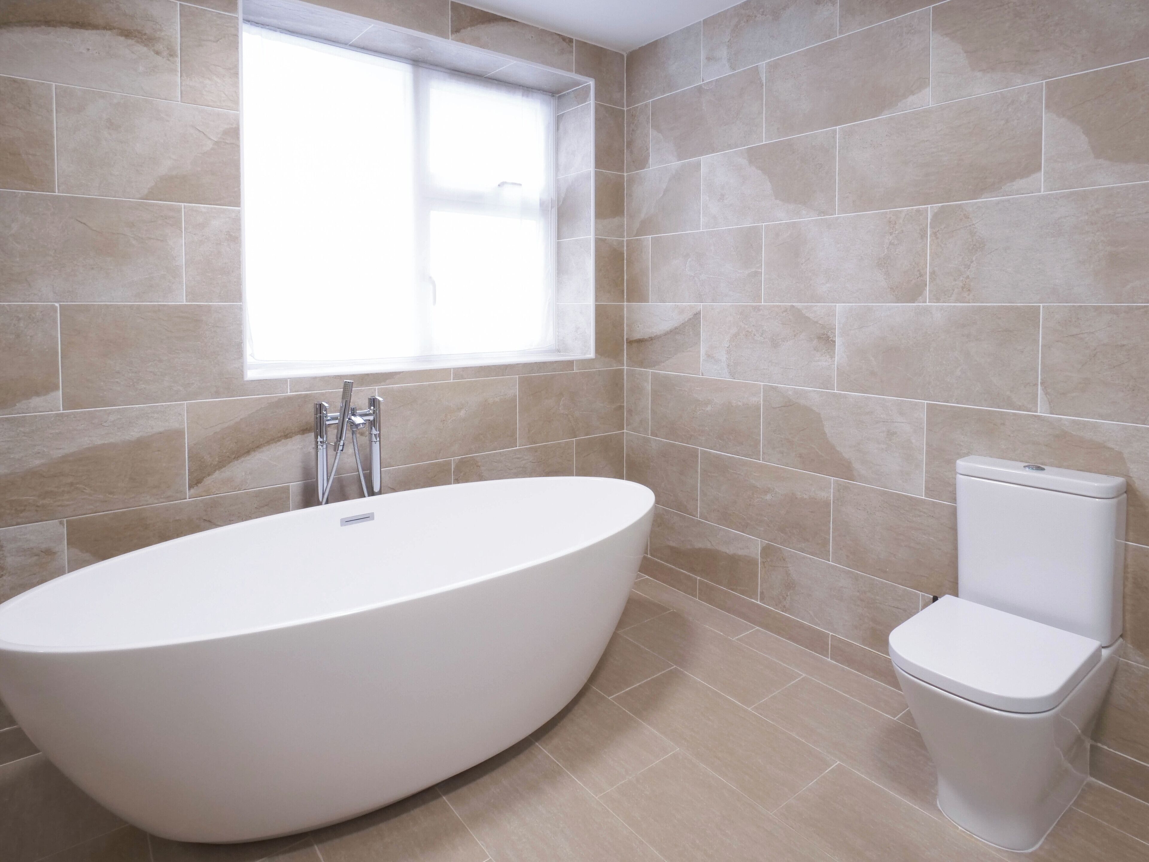 Un bagno moderno con una vasca da bagno indipendente, un water e una finestra che lascia entrare luce naturale.