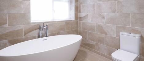 A modern bathroom with a freestanding bathtub, a toilet, and a window providing natural light.