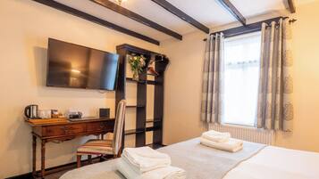 Habitación de hotel con cama, escritorio con televisor de pantalla plana, silla, estante con un florero y ventana con cortinas.