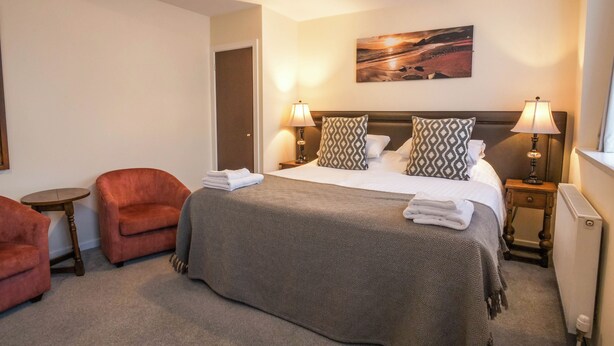 A hotel room with a bed, two bedside lamps, a painting on the wall, a door, and two armchairs. - Black Boy Inn (Caernarfon)