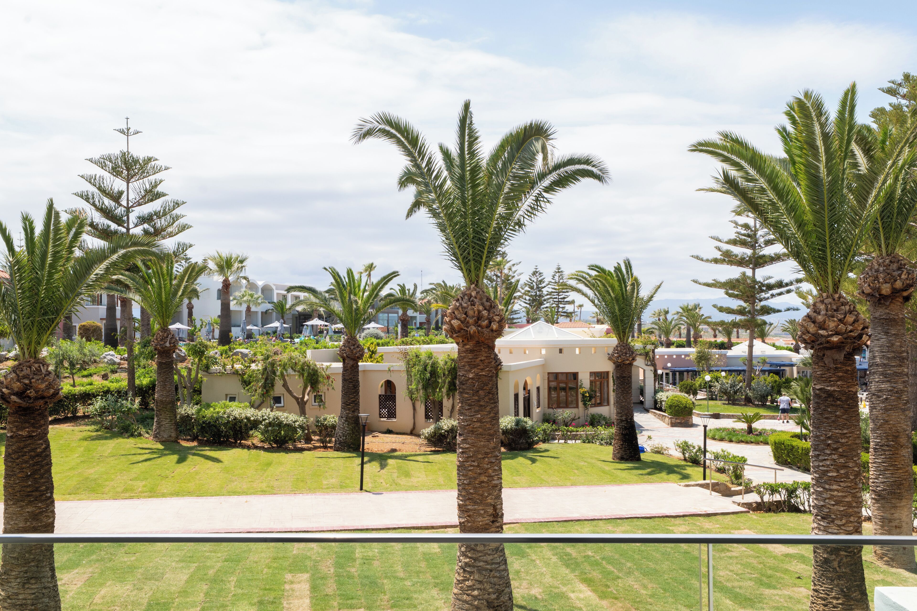Un patio con palmeras, césped y un edificio con ventanales arqueados.
