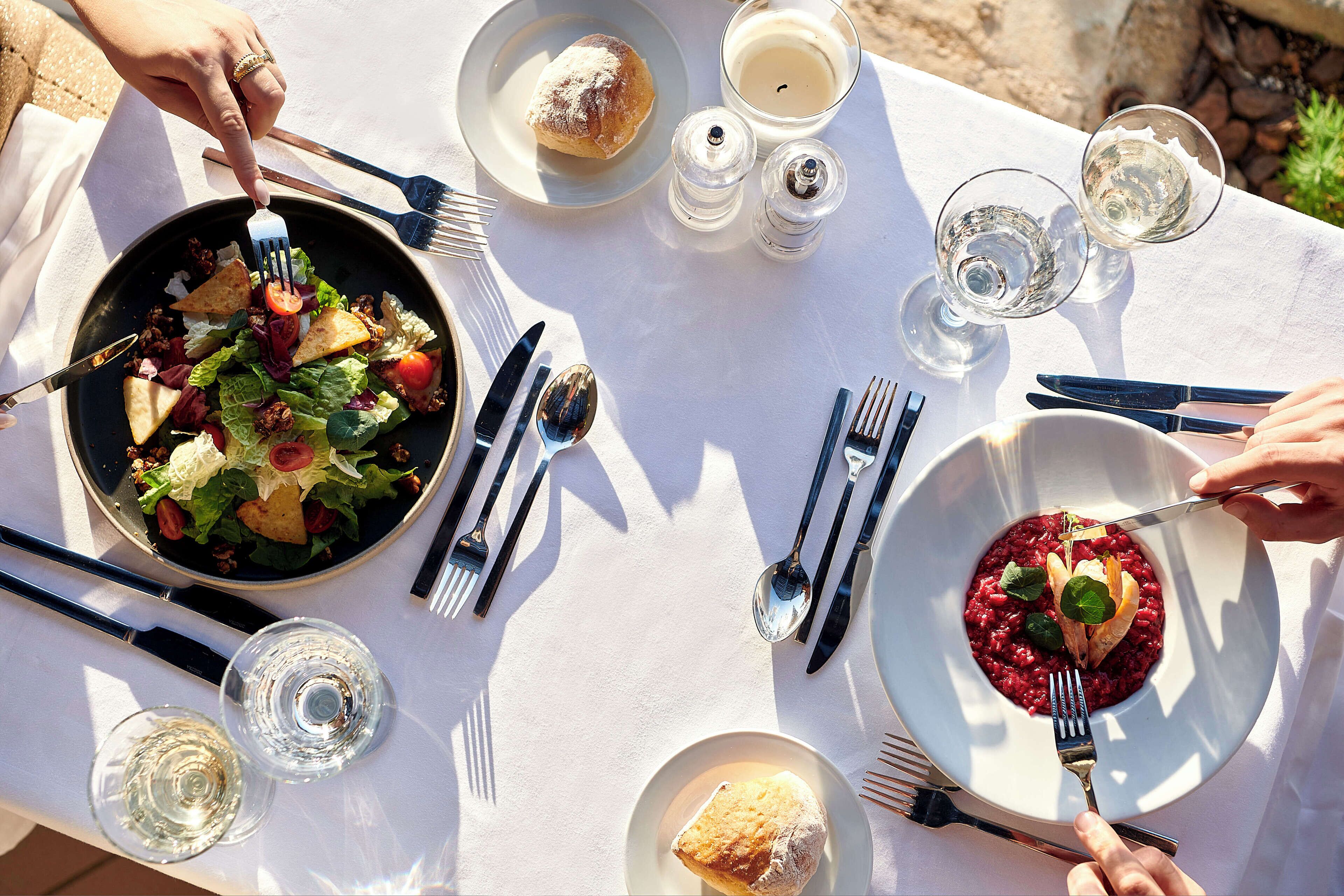 Un tavolo da pranzo con piatti di cibo, posate e bicchieri d'acqua.