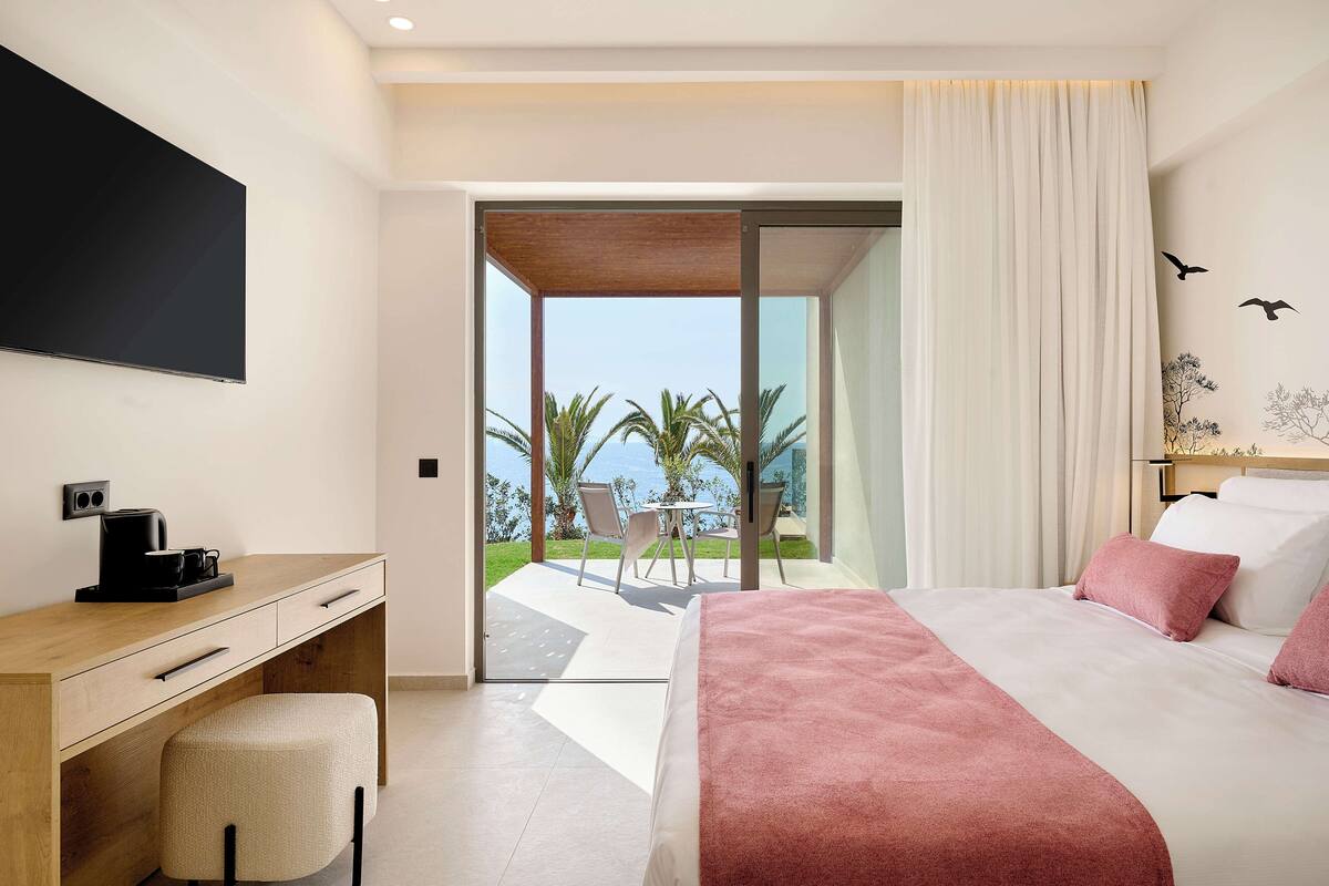 Une chambre d’hôtel moderne dotée d’un grand lit, d’un bureau et offrant une vue sur les palmiers et l’océan.