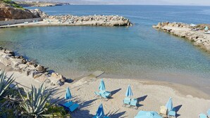 A coastal beach with clear water, rocky breakwaters, and several beach chairs and umbrellas. - Iberostar Waves Creta Panorama & Mare (Mylopotamos)