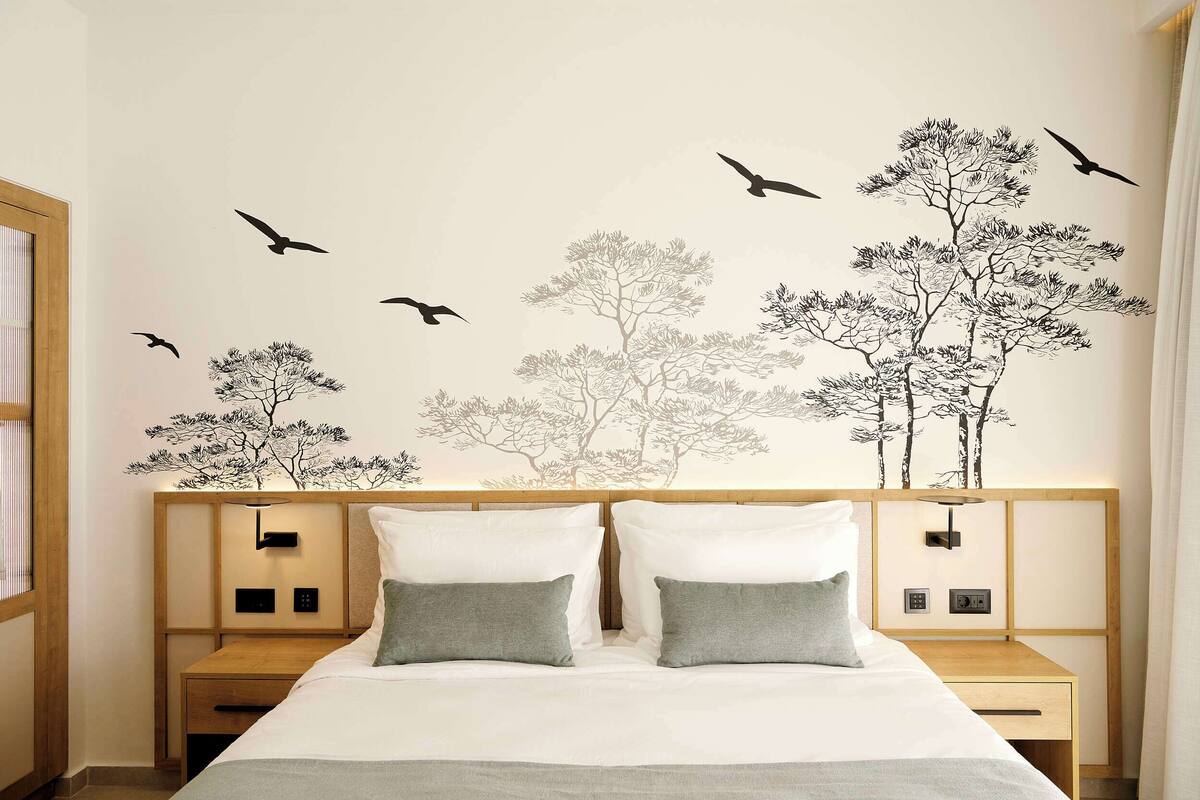 Une chambre d’hôtel avec un lit, deux tables de chevet et un mur décoré d’autocollants représentant des arbres et des oiseaux.