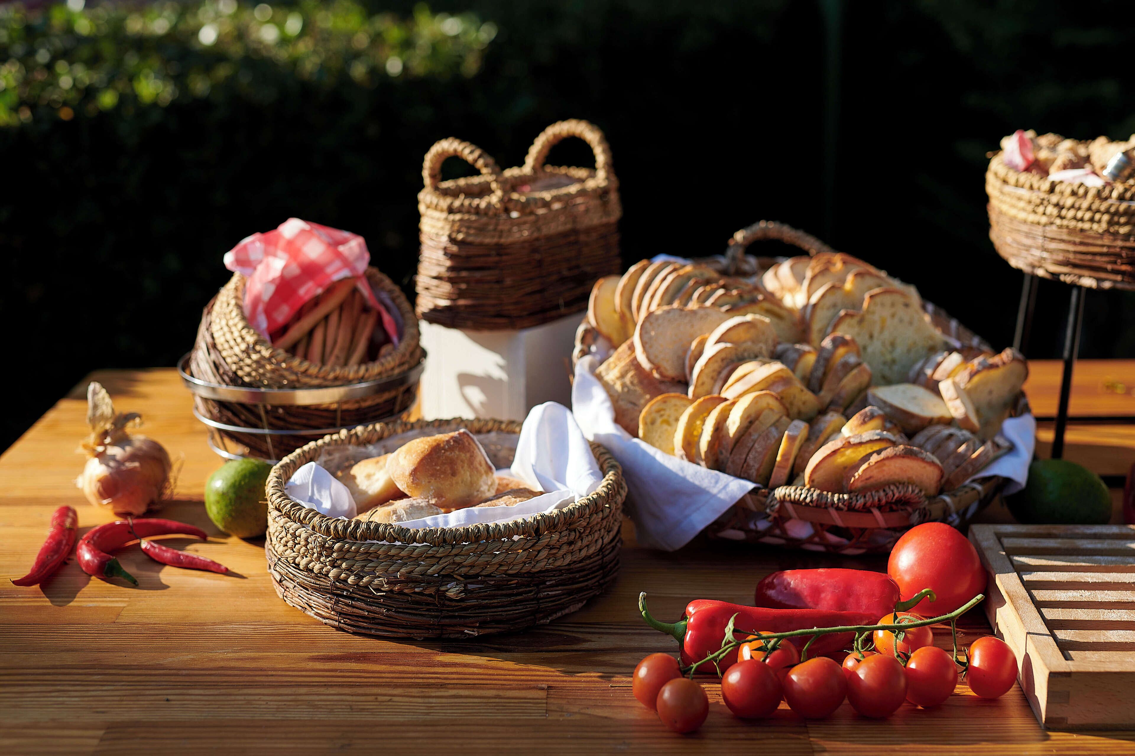 A wooden table with baskets of bread, tomatoes, and chili peppers.