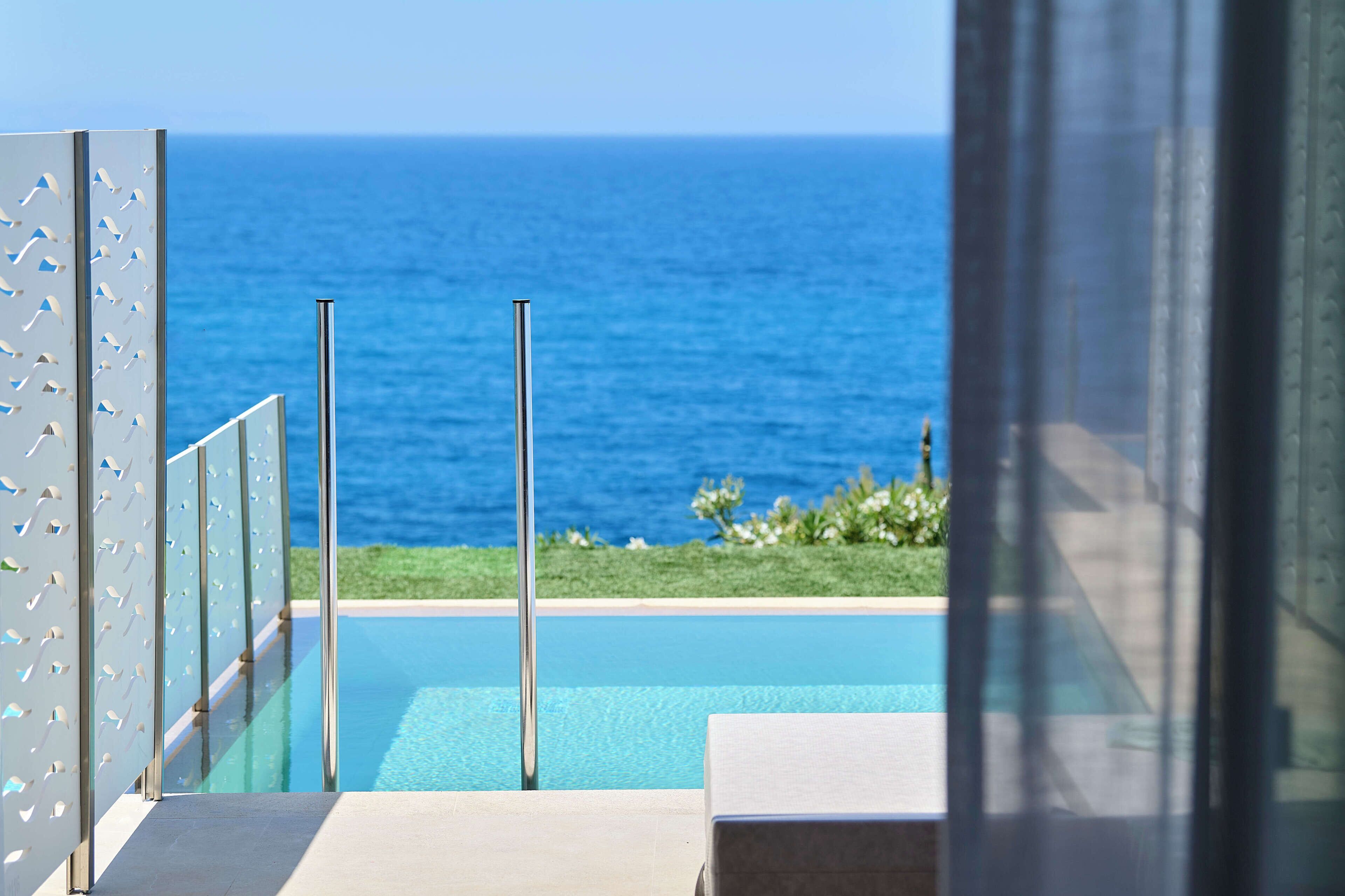 Una zona de piscina moderna amb aigua blava cristal·lina, vista a l'oceà i barana de vidre.