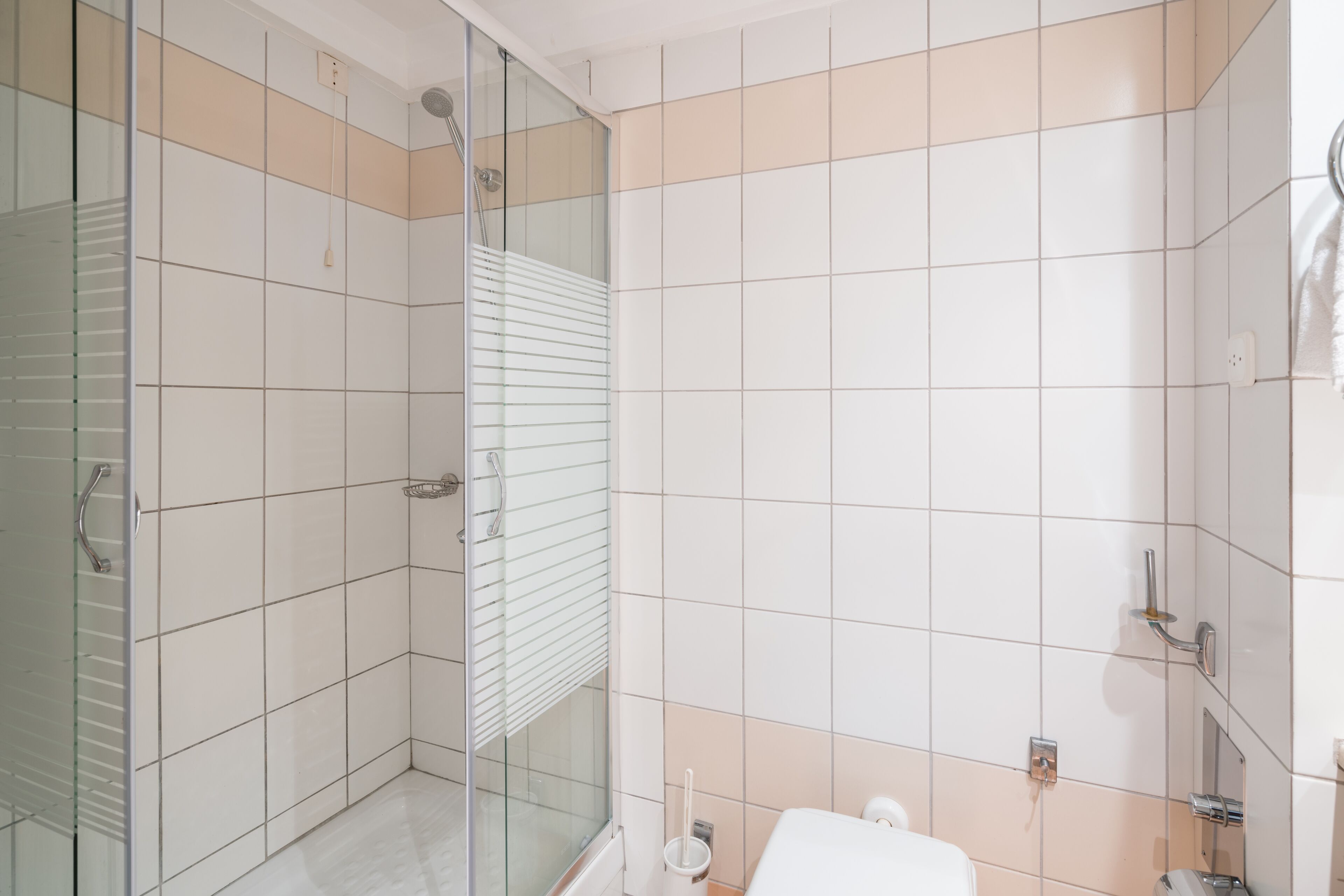 Un baño con cabina de ducha de vidrio, azulejos blancos y un inodoro.