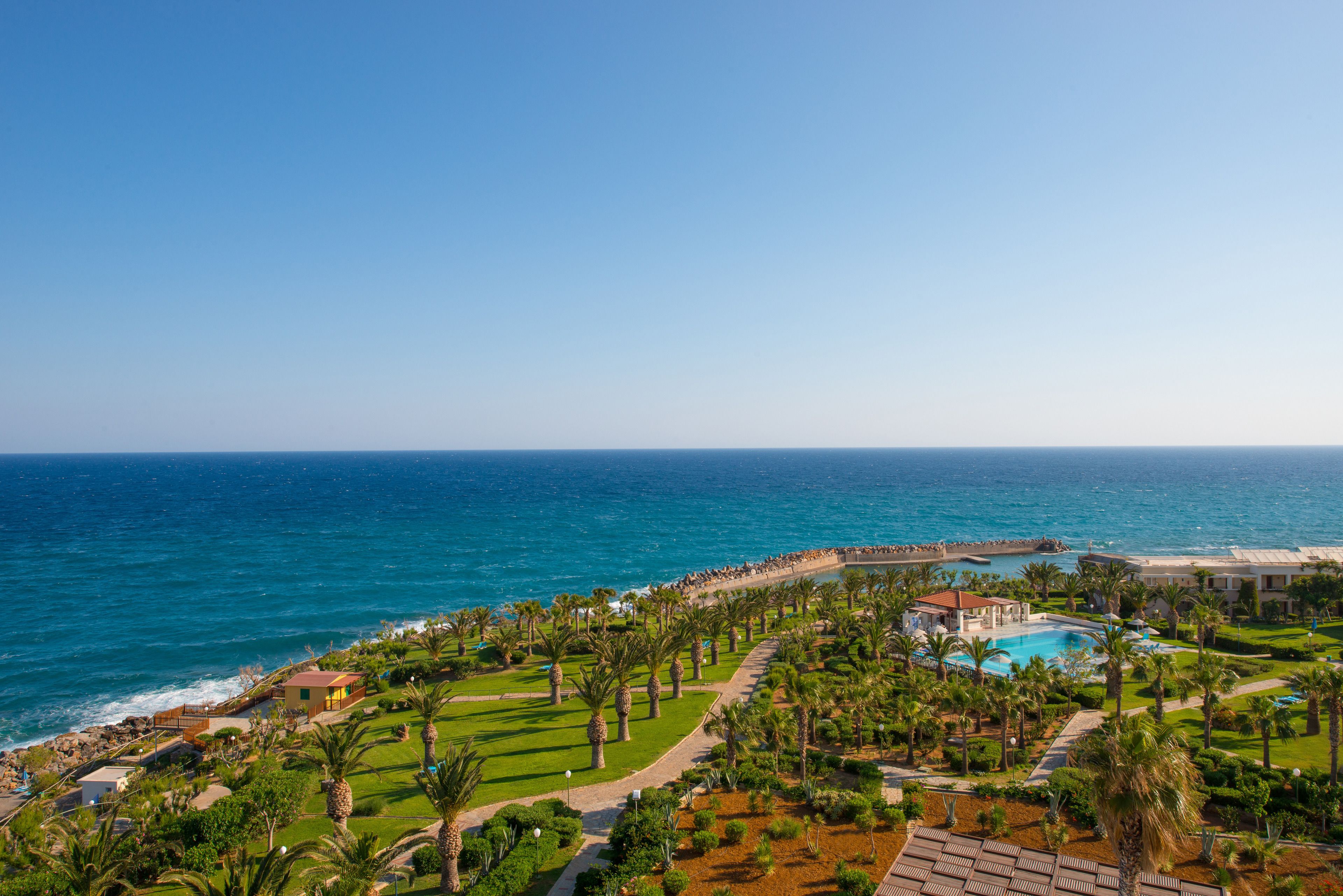 A resort with a pool, palm trees, and a view of the ocean.