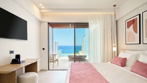 A hotel room with a bed, a desk, a chair, a TV, and a view of the ocean. - Iberostar Waves Creta Panorama & Mare (Mylopotamos)