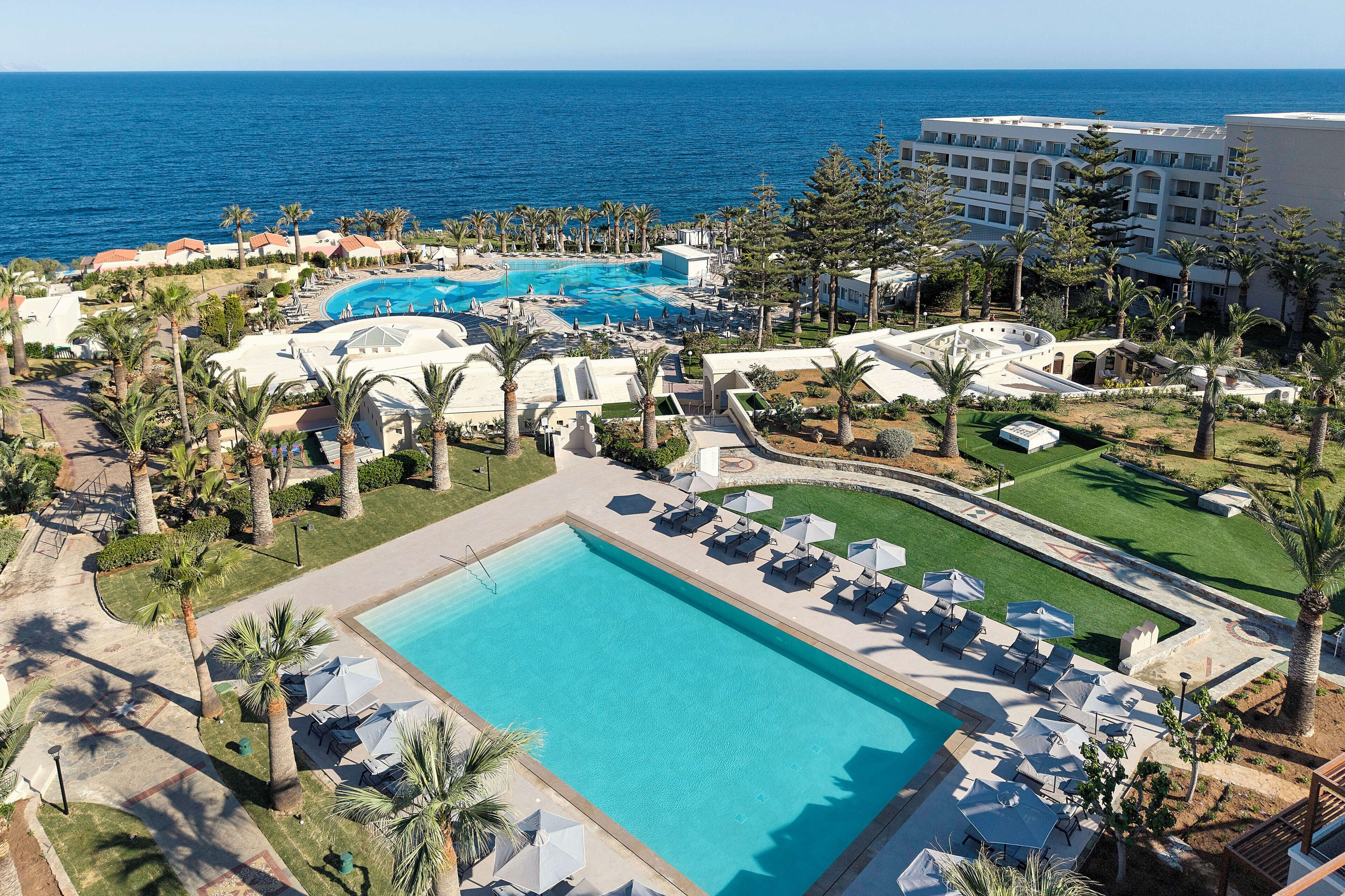 Un resort con varias piscinas, palmeras y vista al océano.